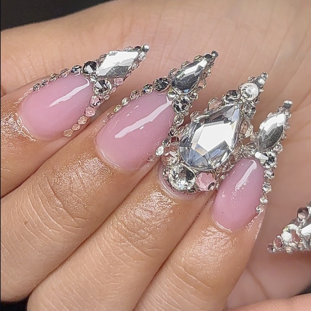Long almond-shaped Gel-X nails with a glossy pink nude finish and dramatic crystal embellishments by n4ilsbybellaa